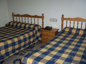 Un dormitorio con dos camas, cada una con una colcha a cuadros, un cabecero de madera y una mesita de noche con teléfono.