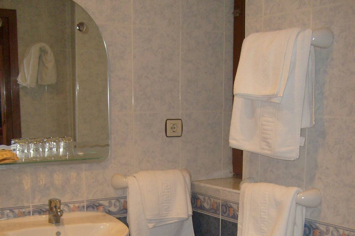 Un baño con lavamanos, inodoro y varias toallas colgadas en toalleros.