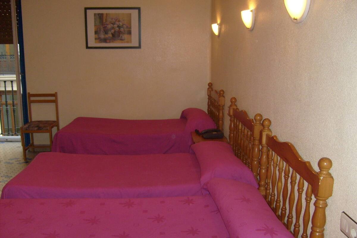 Una habitación con dos camas, una silla y un cuadro en la pared.