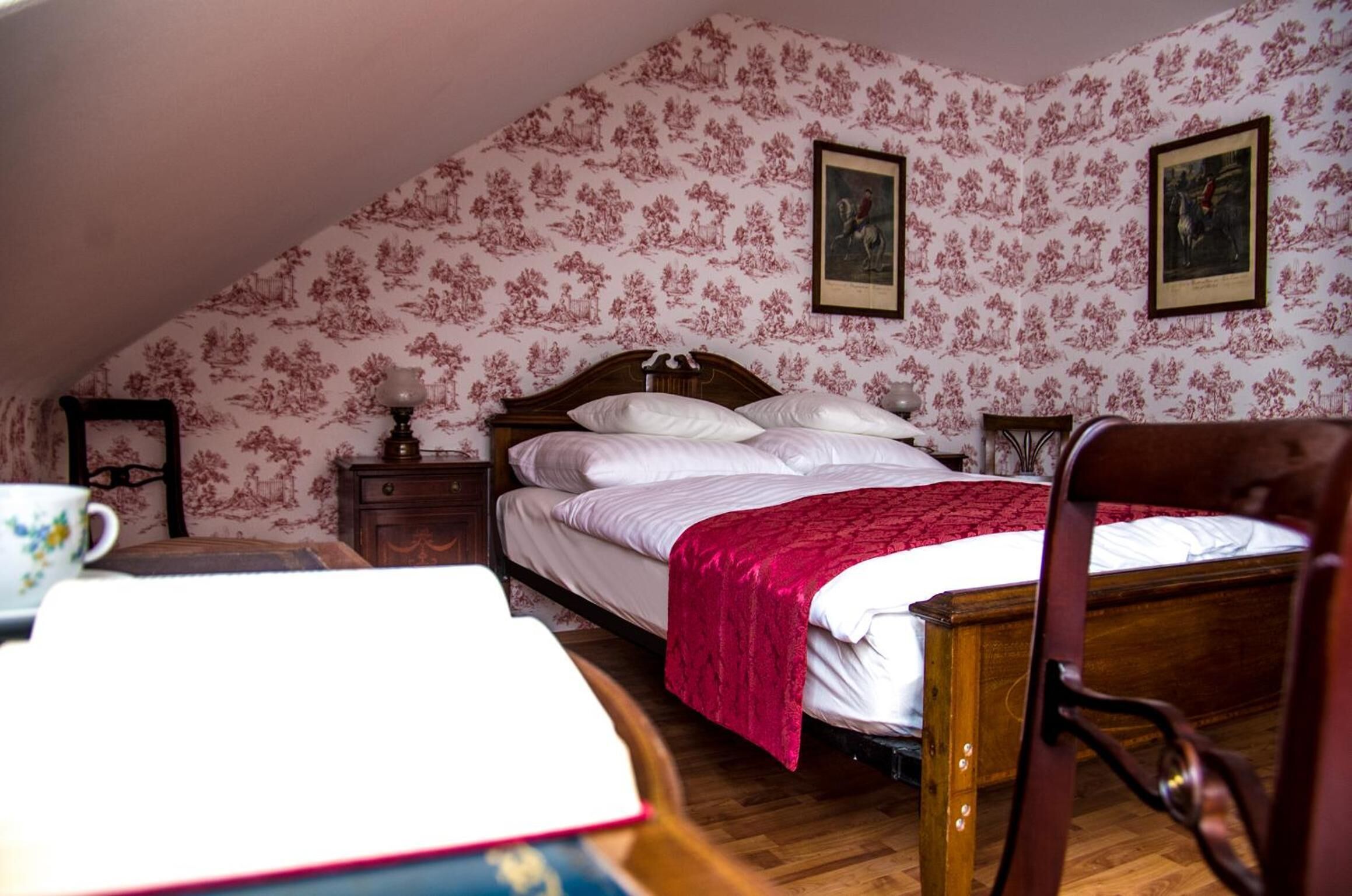 Une chambre à coucher avec un lit en bois, un papier peint à motifs floraux et deux tableaux encadrés accrochés au mur.