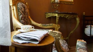 A room with a vintage chair, a small table with a cup and a book, a mirror, and a bed. - Hotel Victoria (Schlangenbad)