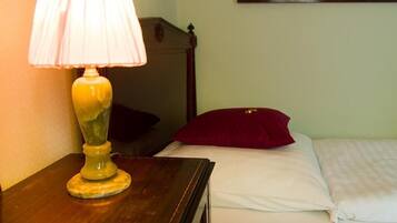 A wooden nightstand with a lamp, a bed with white bedding and a red pillow, and a wooden headboard.