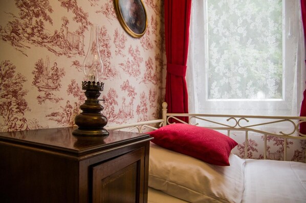A bedroom with a bed, a nightstand, a lamp, and a window with a view of trees.
