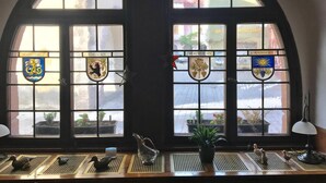A room with a large arched window displaying four coats of arms, a small table with decorative items, and a potted plant. - Gasthof Bären Ochsenfurt (Ochsenfurt)