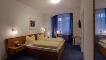 A hotel room with a double bed, bedside tables, a desk, a chair, a mirror, and a picture on the wall.
