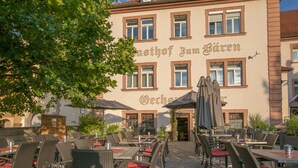 An outdoor cafe with wicker tables and red cushions, set against a building with the sign "Gasthof Zum B ären". - Gasthof Bären Ochsenfurt (Ochsenfurt)