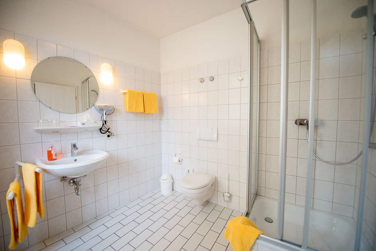 A modern bathroom with a white sink, mirror, and toilet, a shower area, and yellow towels.