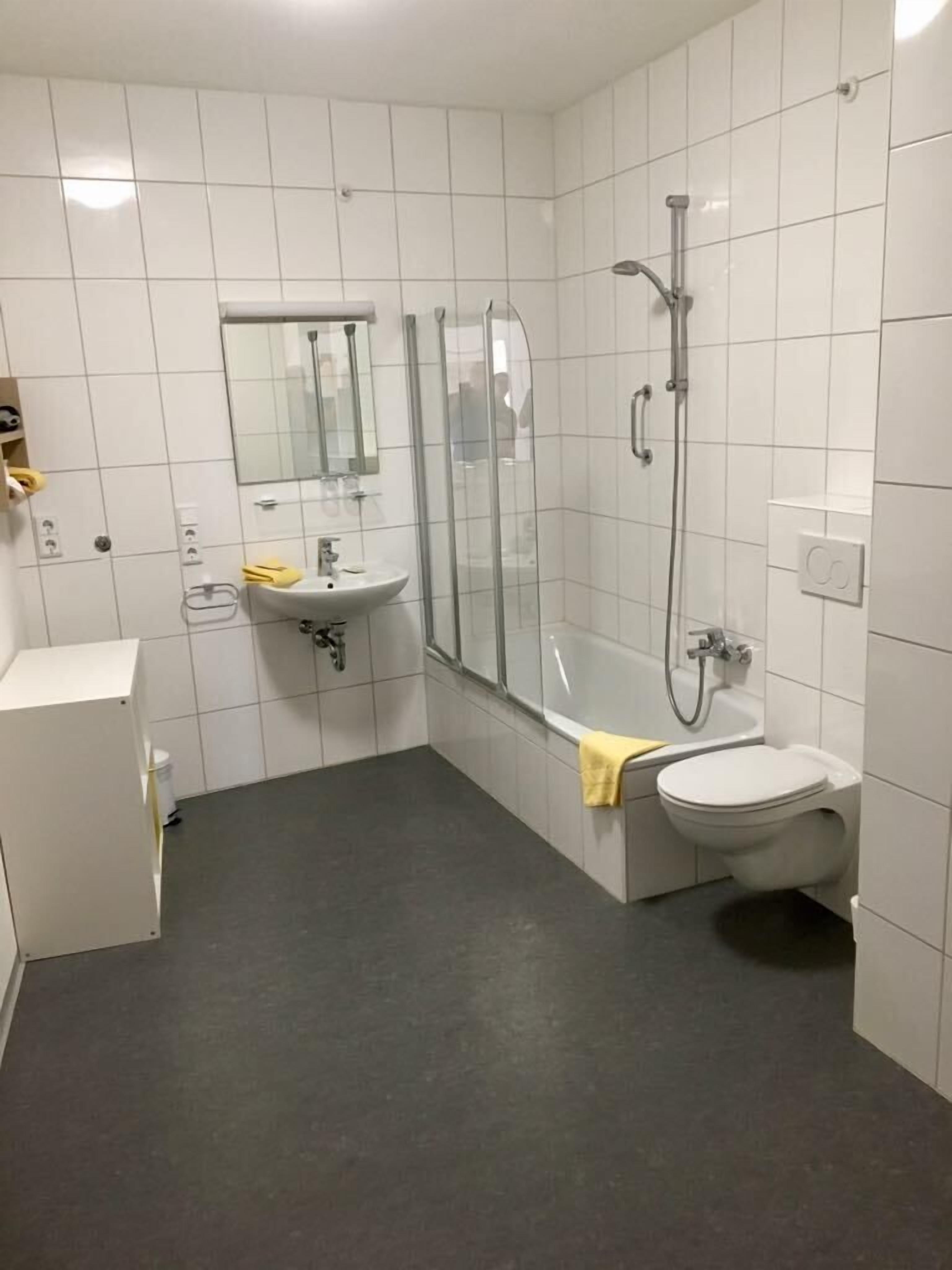 A modern bathroom with white tiles, a glass-enclosed shower, a sink, and a toilet.