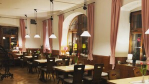 A restaurant with wooden flooring, multiple tables and chairs, and hanging pendant lights. - Gasthof Bären Ochsenfurt (Ochsenfurt)