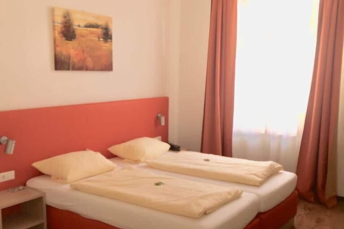 A double bed with a red headboard, a bedside table, and a painting on the wall.