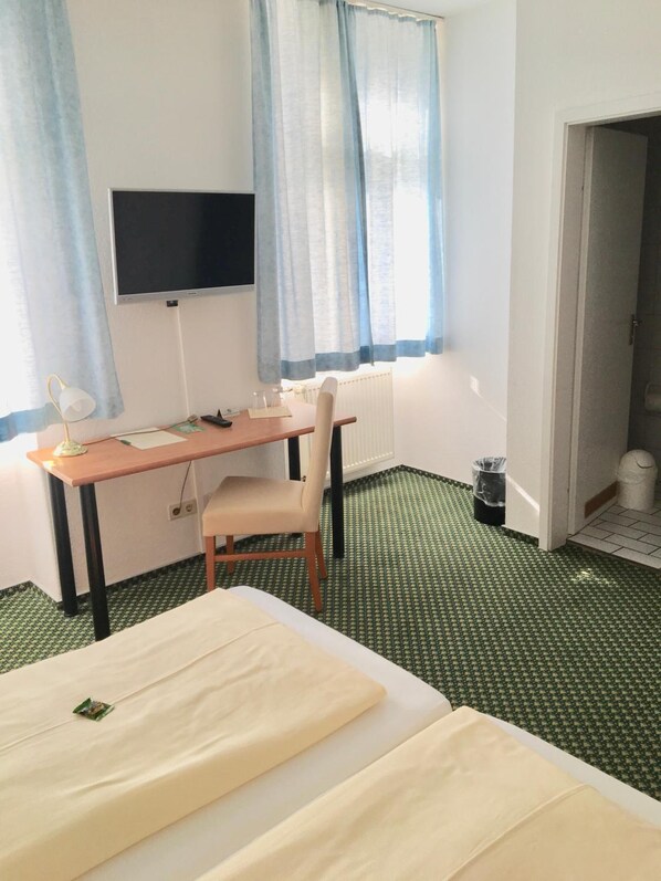 Una habitación de hotel con cama, escritorio con silla, televisión y ventana con cortinas.