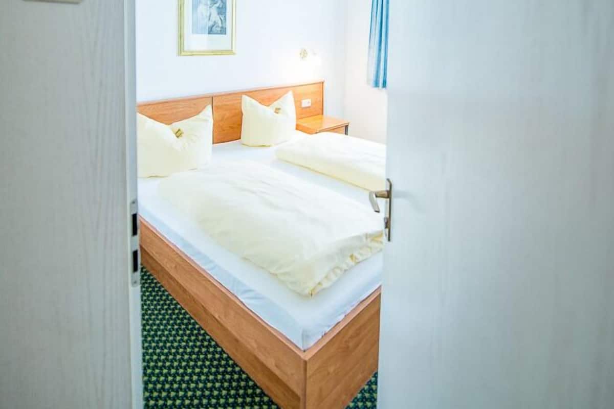 A hotel room with a bed, a nightstand, a framed picture on the wall, and a number on the door.