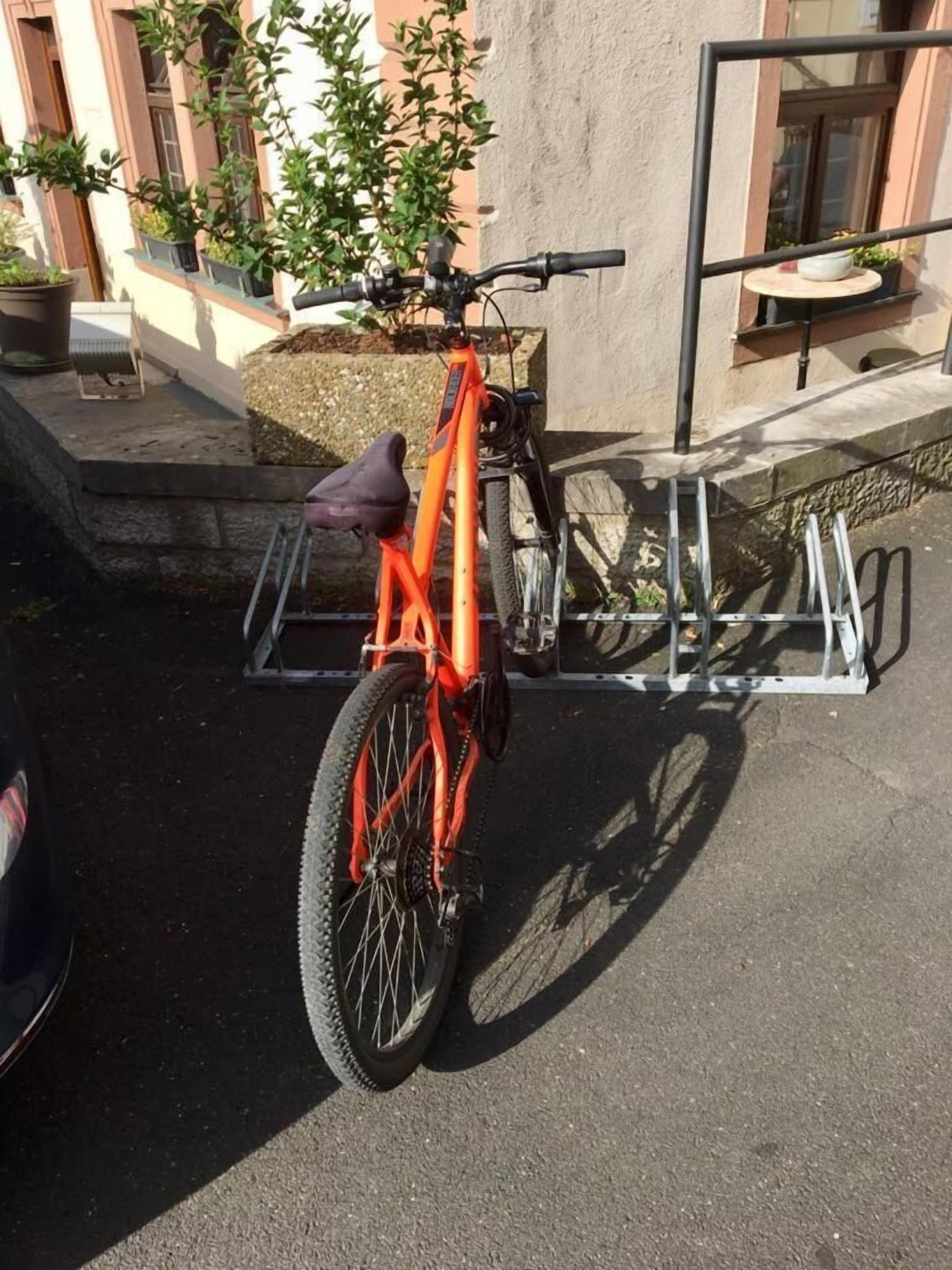 Una bicicleta estacionada sobre una superficie de concreto con un soporte metálico adosado a un edificio.