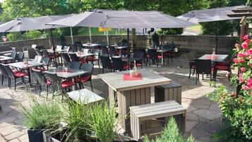 An outdoor patio with tables and chairs, umbrellas, and potted plants.