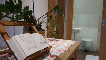 Une salle de bain avec une chaise en bois, une plante en pot et un livre posé sur une table.