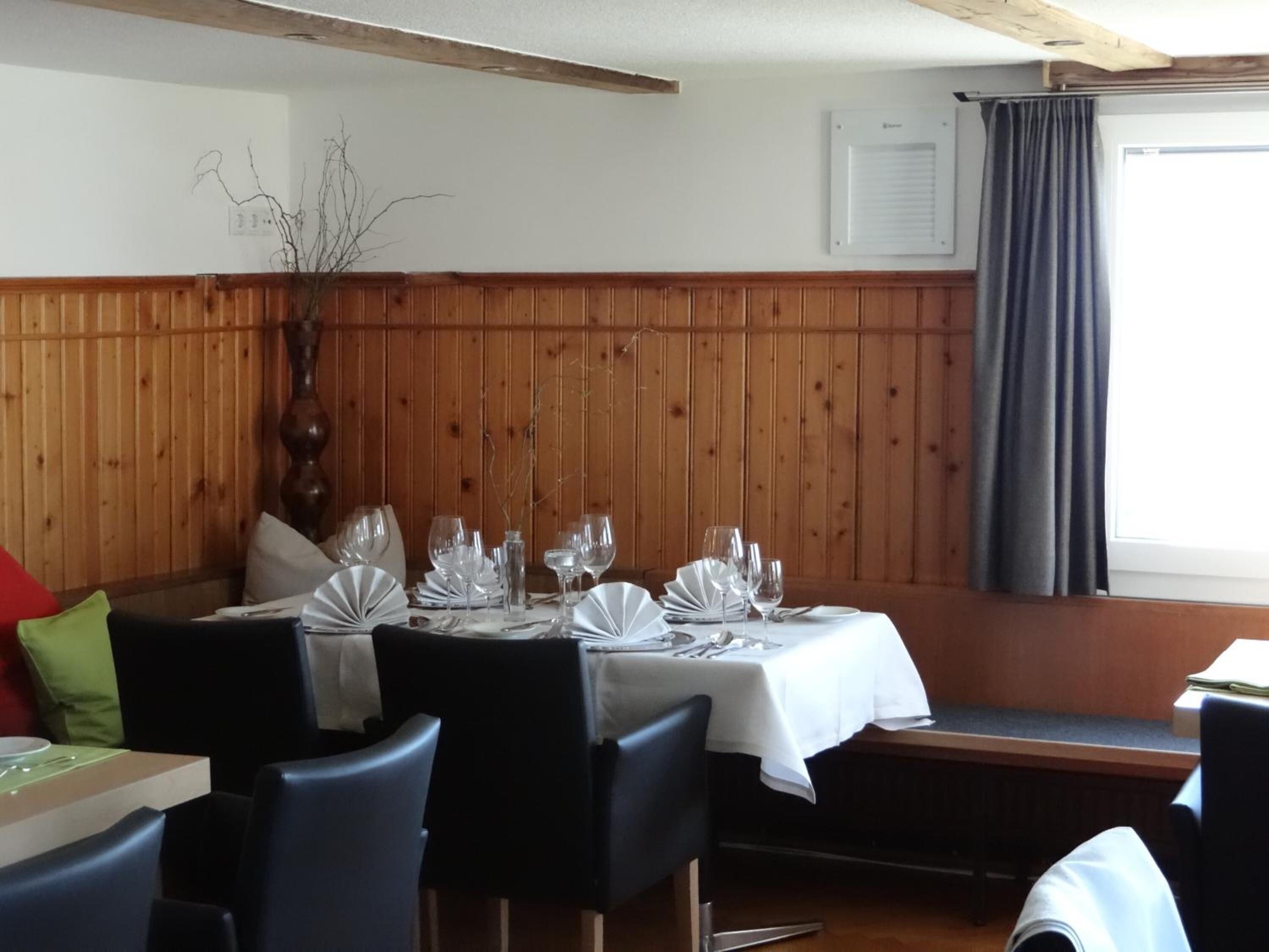 A restaurant with wooden paneling, a white tablecloth-covered table set for four, and a window with a curtain.