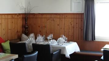 A restaurant with wooden paneling, a white tablecloth-covered table set for four, and a window with a curtain.