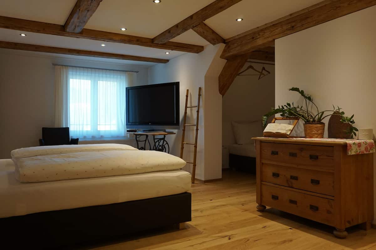 Un dormitorio con cama, cómoda de madera, televisor y ventana con cortinas.