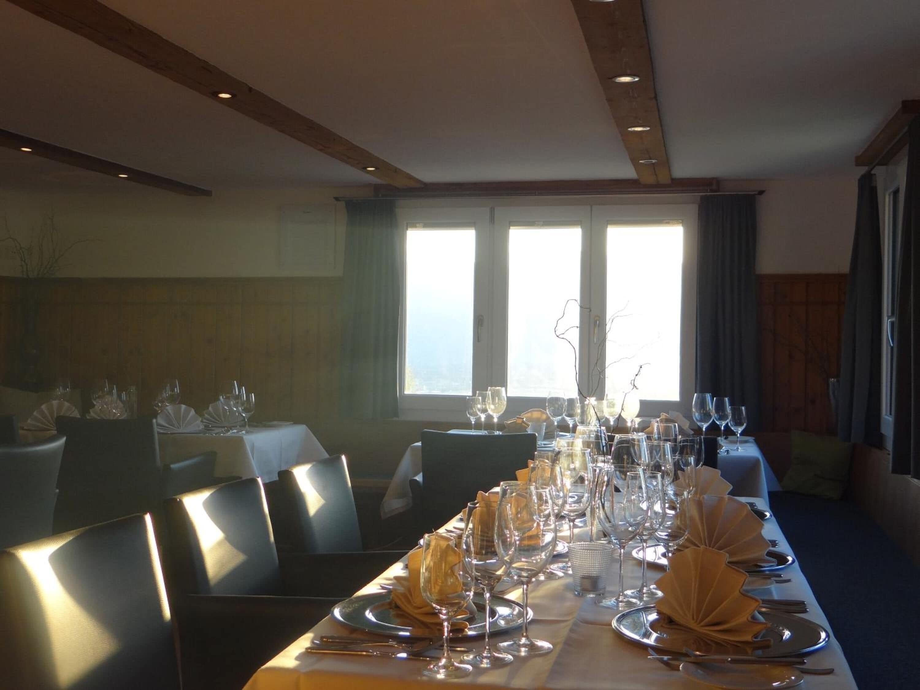 A dining area with a long table set for a meal, large windows, and a view of the outdoors.
