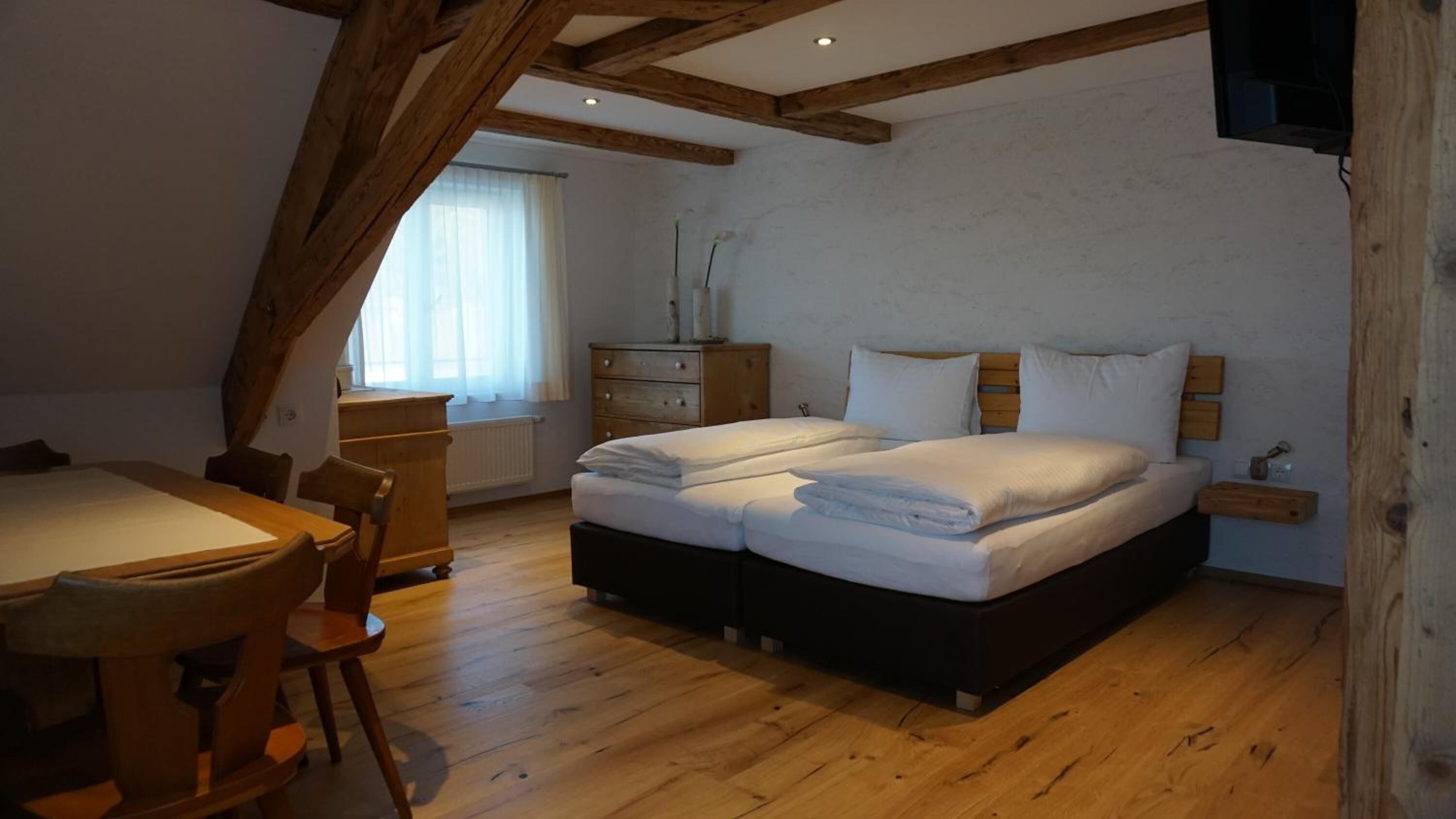 A bedroom with a wooden ceiling, a bed with white linens, a wooden dresser, and a window with curtains.