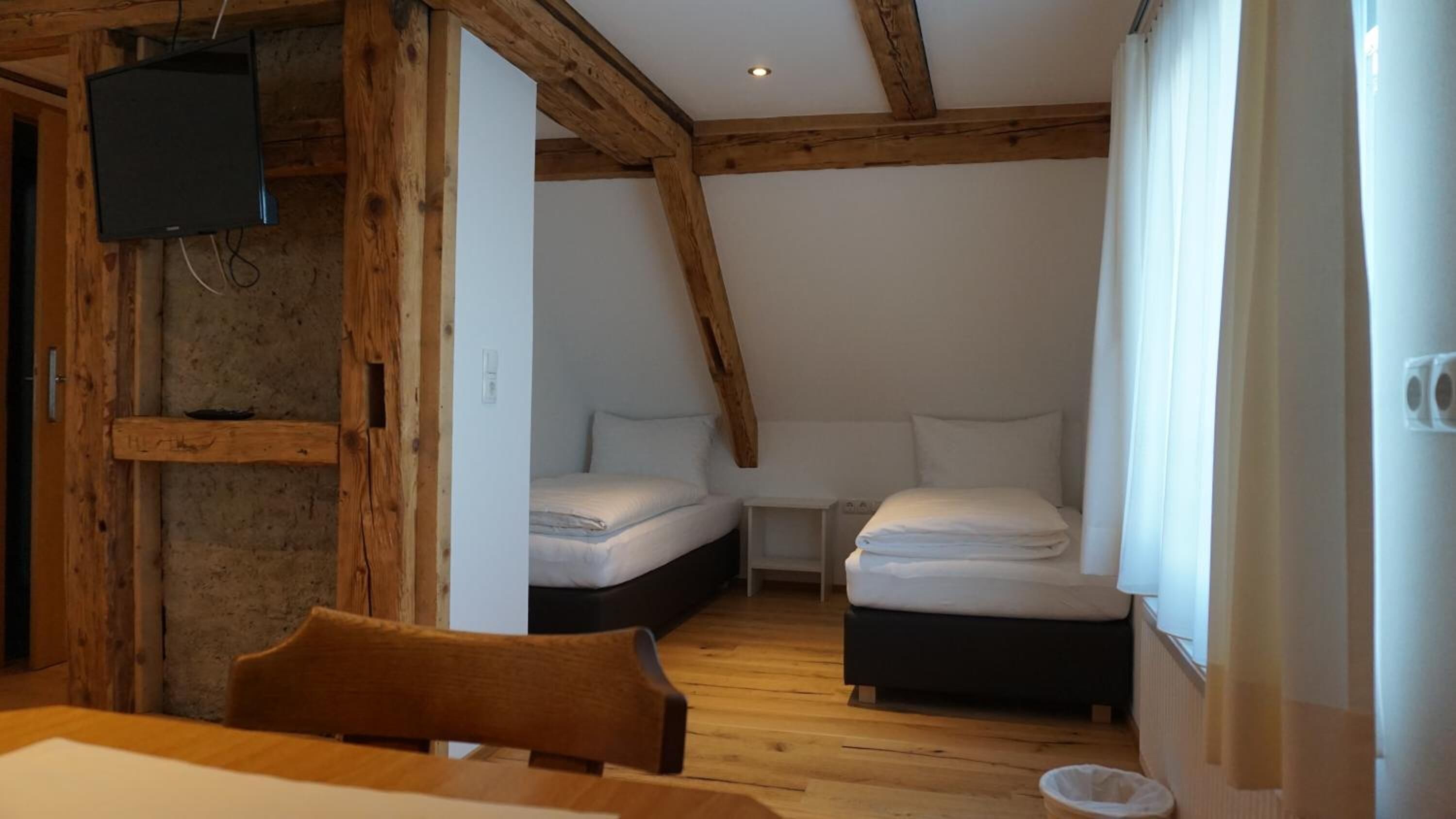 Une petite pièce rustique avec des poutres en bois, deux lits, une télévision et une table.