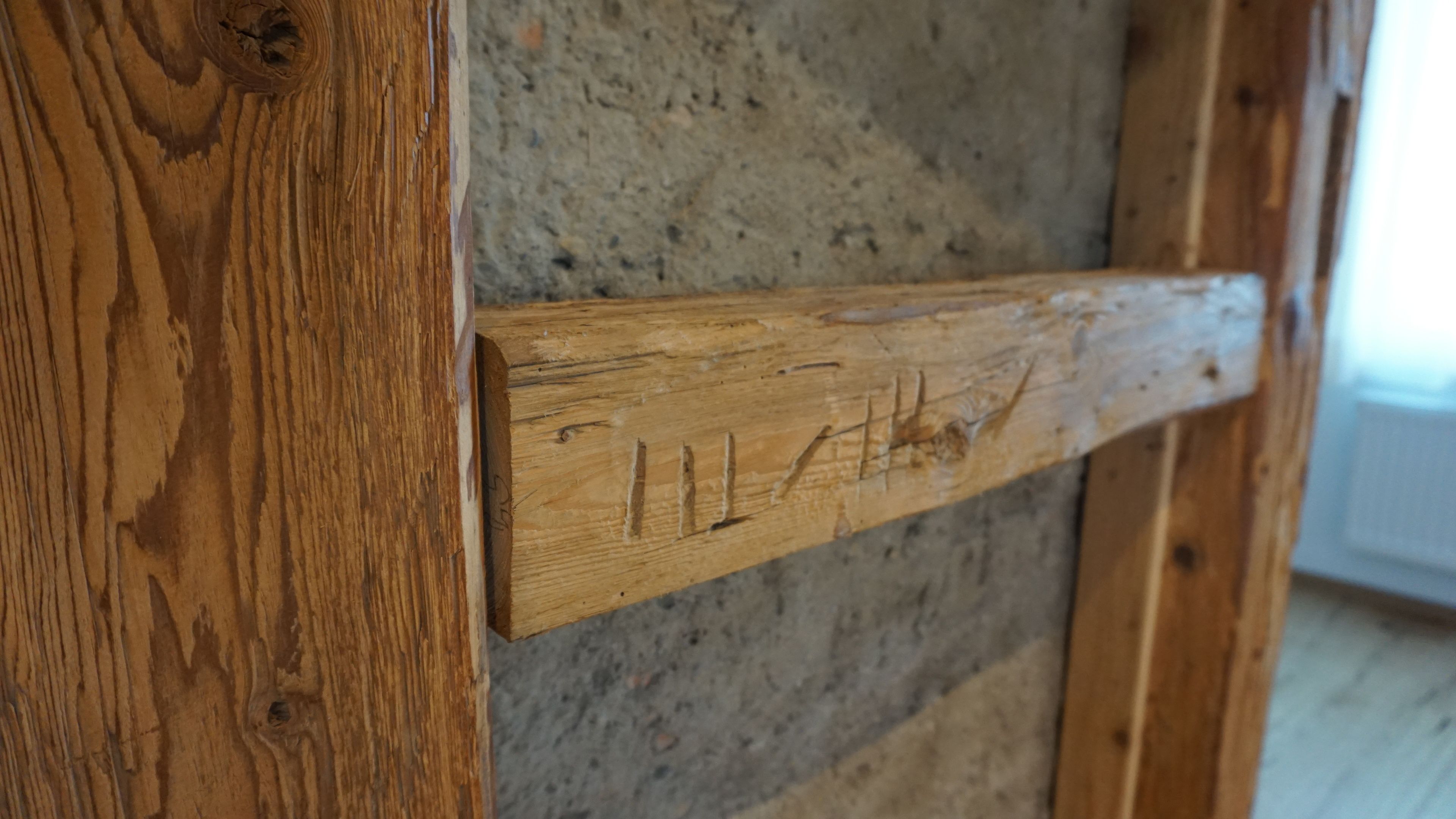 Ein verwitterter Holzbalken, befestigt an einer rauen Steinwand.