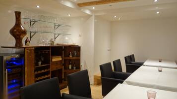 Un comedor con una mesa larga, sillas negras, un estante de madera con cristalería y un jarrón decorativo.