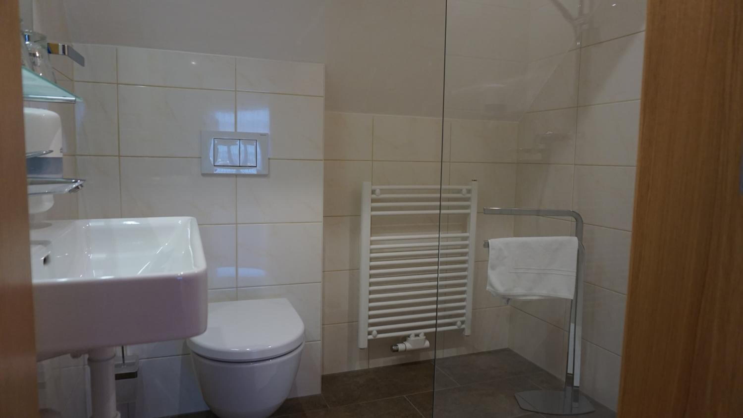 A small, clean bathroom with a white sink, toilet, and a glass shower enclosure.