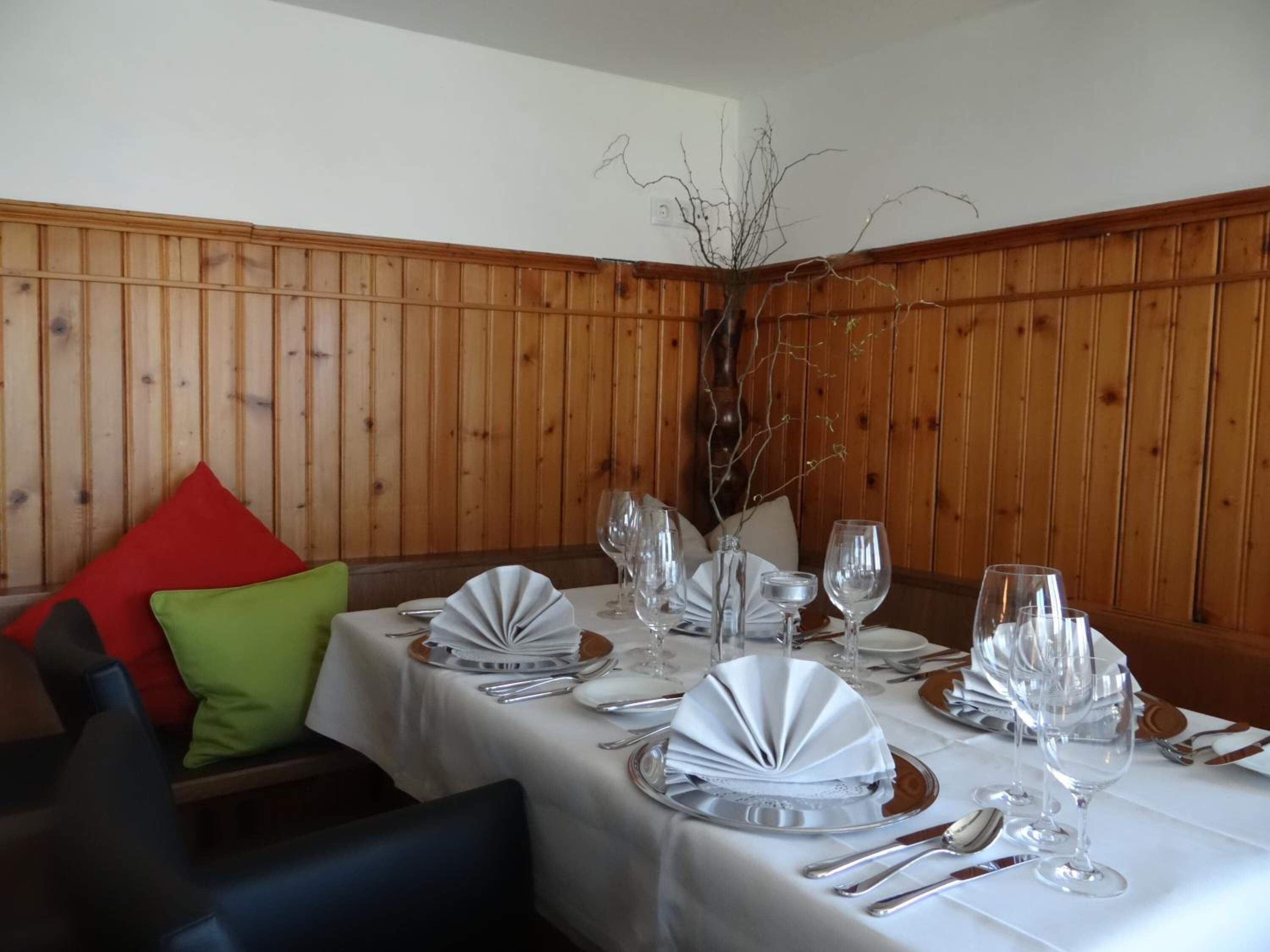 A dining table set with white tablecloths, silverware, and wine glasses, with a wooden paneled wall in the background.