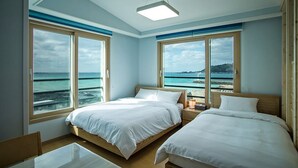 A hotel room with two beds, large windows with ocean views, and a small table. - Sleep in the Sea (Jeju City)