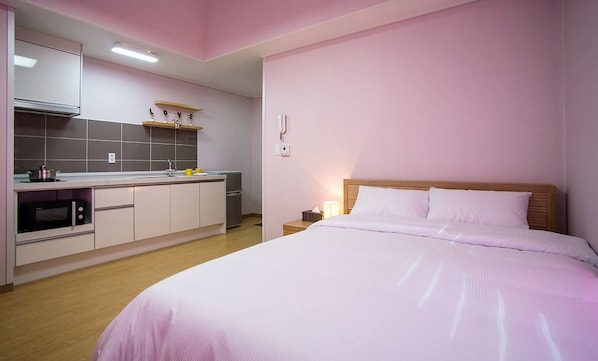 A bedroom with a large bed, a bedside table, a nightstand, and a kitchenette area with a microwave, stove, and cabinets. - Sleep in the Sea (Jeju City)