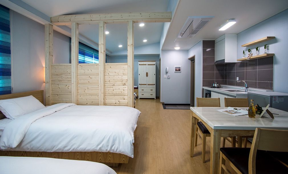 A hotel room with a wooden bed, a small dining table, and a kitchenette.