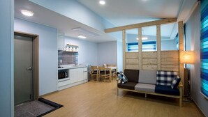 A modern kitchen with white cabinets, a dining area with a table and chairs, and a sofa with a plaid cushion. - Sleep in the Sea (Jeju City)