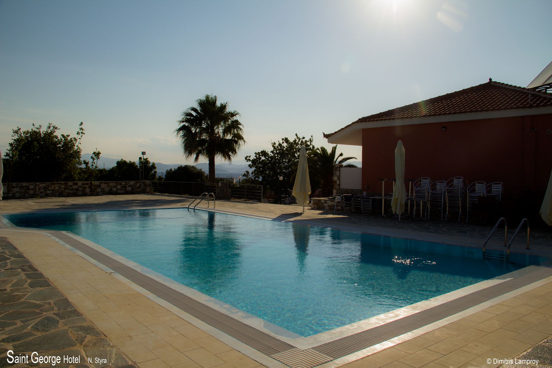 Una piscina con solárium de baldosas, una palmera y un edificio con terraza.