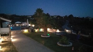 Una vista notturna di una località turistica con vialetti, palme e aree salotto all'aperto.