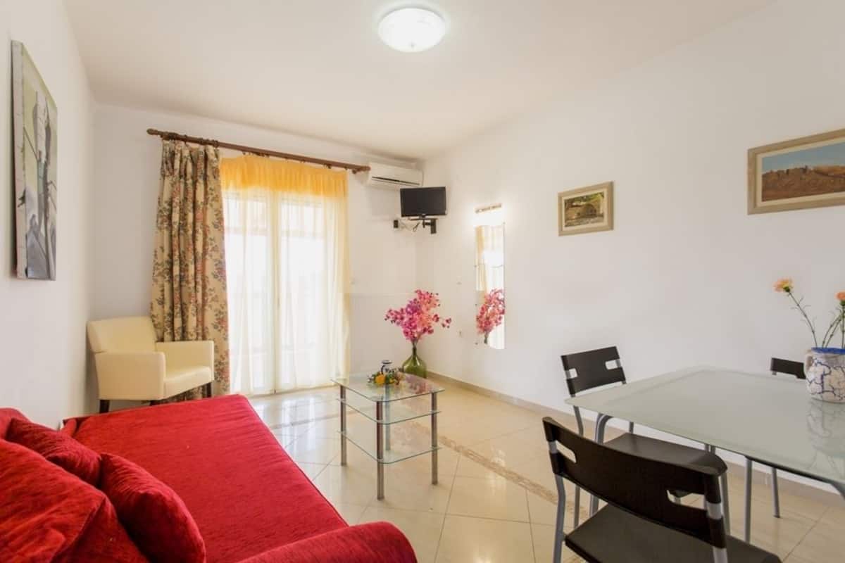 A living room with a red sofa, a glass coffee table, and a dining area with a glass table and chairs.