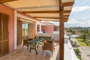 A balcony with a table and chairs, overlooking a garden and distant landscape.
