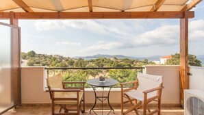 Un balcone con una pergola in legno, due sedie di legno, un tavolino rotondo e vista su un paesaggio collinare.