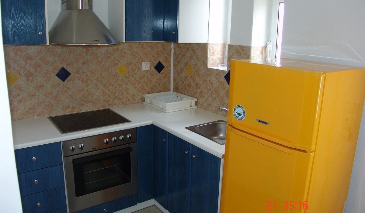 Una cocina con armarios azules, un refrigerador amarillo, una estufa y un lavamanos.
