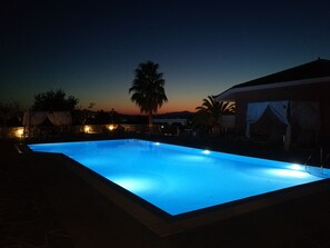 A swimming pool at dusk with a sunset in the background.