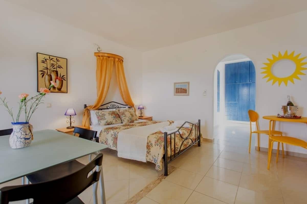 A bedroom with a bed, a table, chairs, a sun decoration, and a painting on the wall.