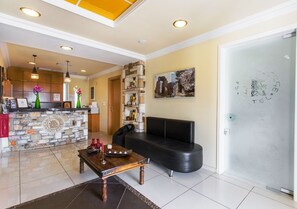 A modern hotel lobby with a stone reception desk, a black leather sofa, and a dining table with candles.