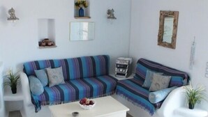 A modern living room with a striped sofa, a white coffee table, and a small side table. - Nakos Homes (Paros)