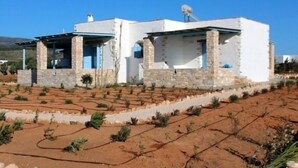 A modern two-story house with stone and white exterior walls, a flat roof, and satellite dishes. - Nakos Homes (Paros)