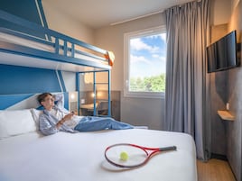 Habitación de hotel con literas, un escritorio, una silla, un televisor y una raqueta de tenis sobre la cama.
