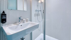 A modern bathroom with a white sink, a glass shower enclosure, and a grid-patterned tiled wall. - ibis budget Orly Chevilly Tram 7 (Chevilly-Larue)