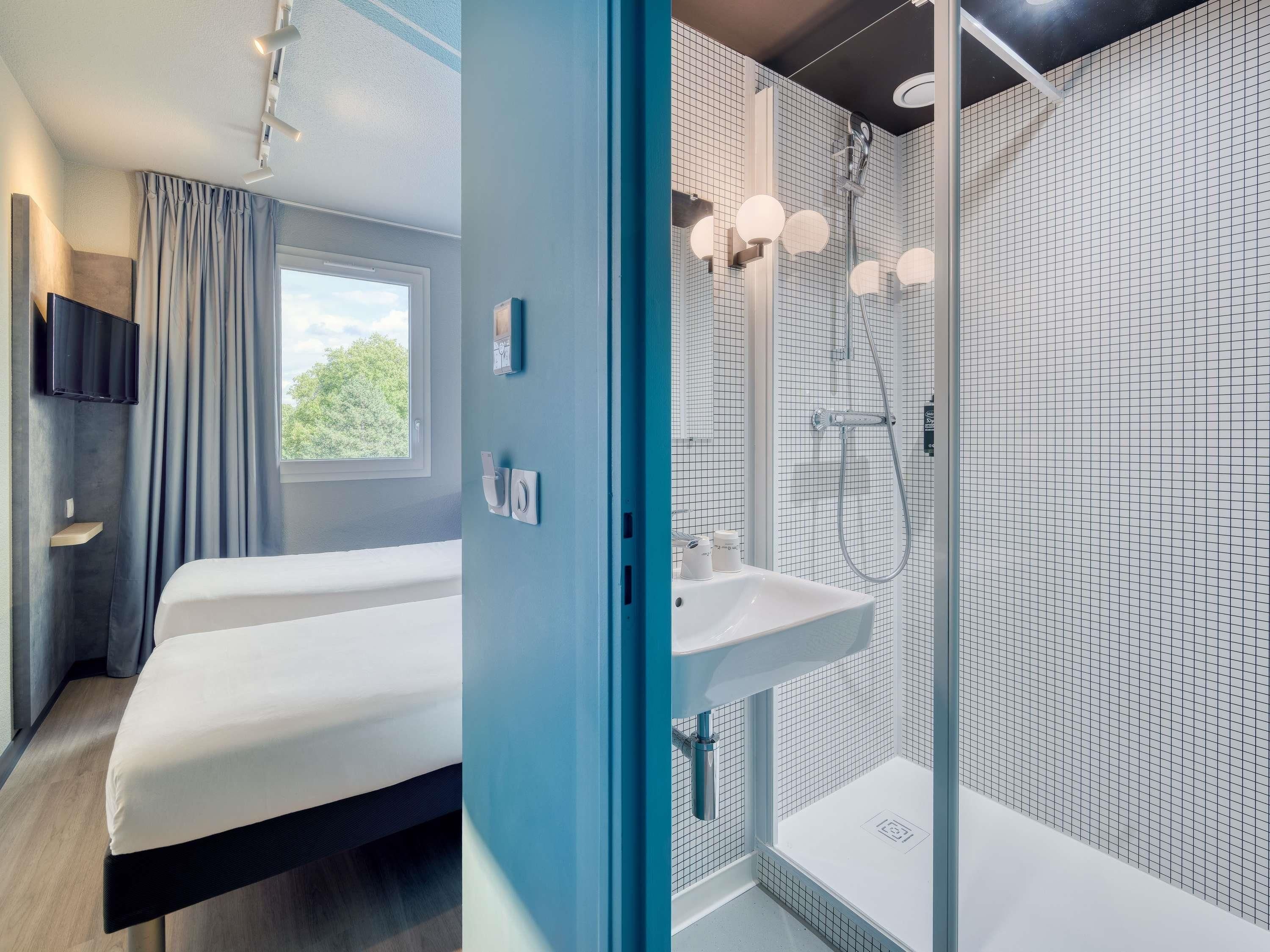 Una habitación de hotel moderna con una cama, un baño con ducha y un ventanal con vistas a zonas verdes.