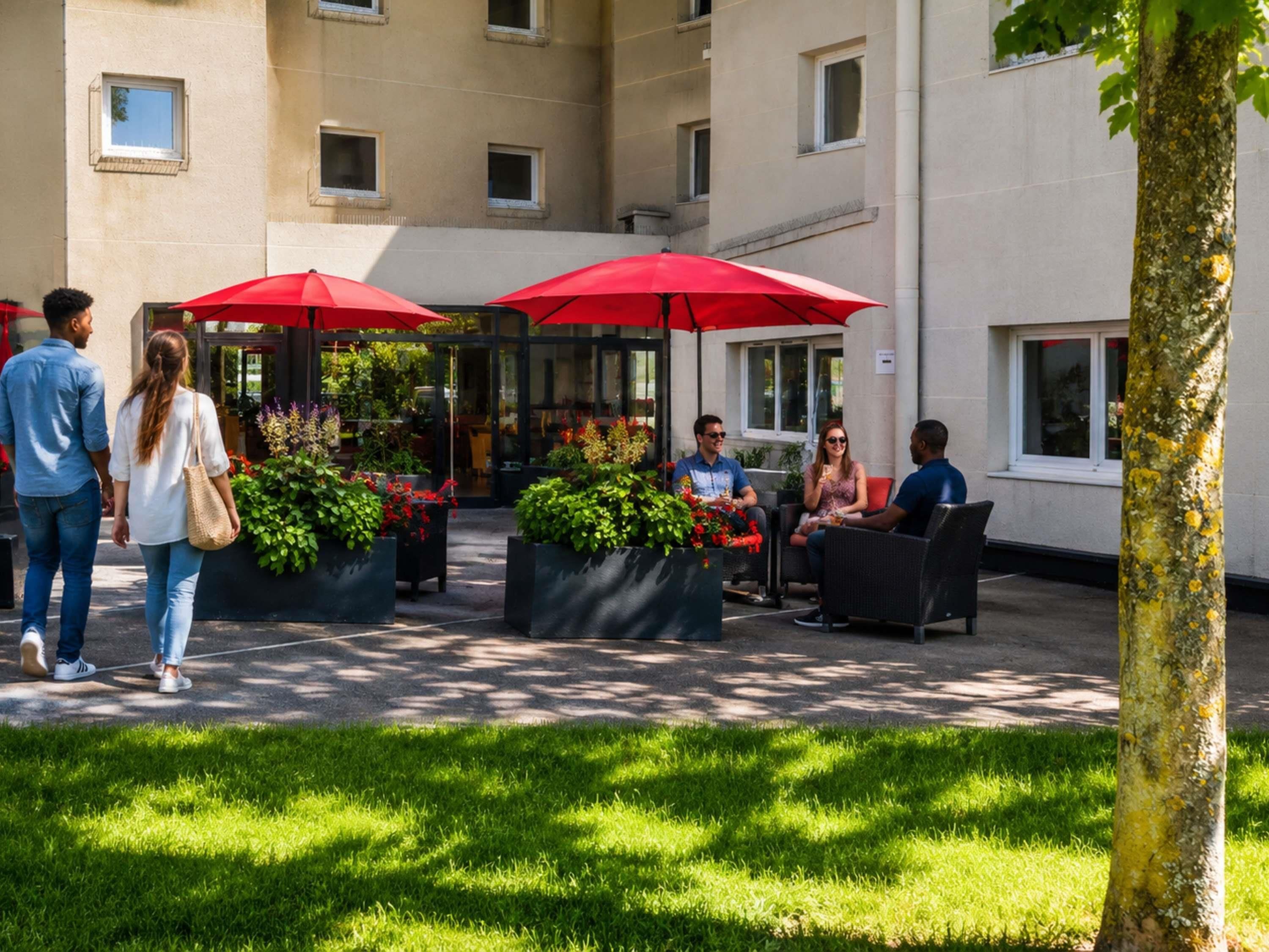 An outdoor seating area with red umbrellas, potted plants, and a building in the background.