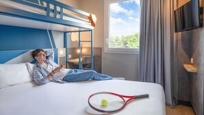 Hotelkamer met een stapelbed, bureau, stoel, televisie en een tennisracket op het bed.