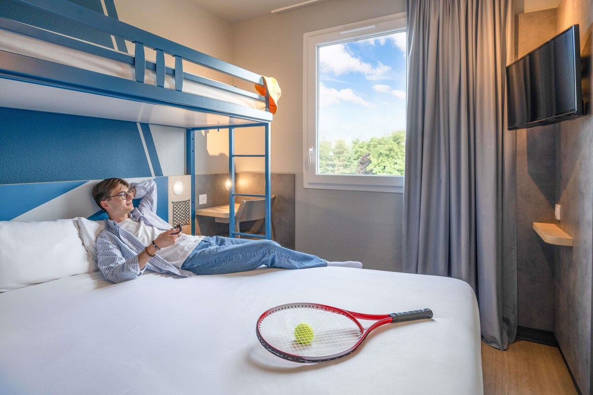 A hotel room with a bunk bed, a desk, a chair, a TV, and a tennis racket on the bed.